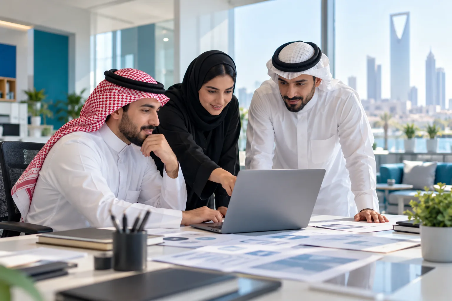 A small Saudi sales team reviewing a shared customer list on a laptop in a bright office