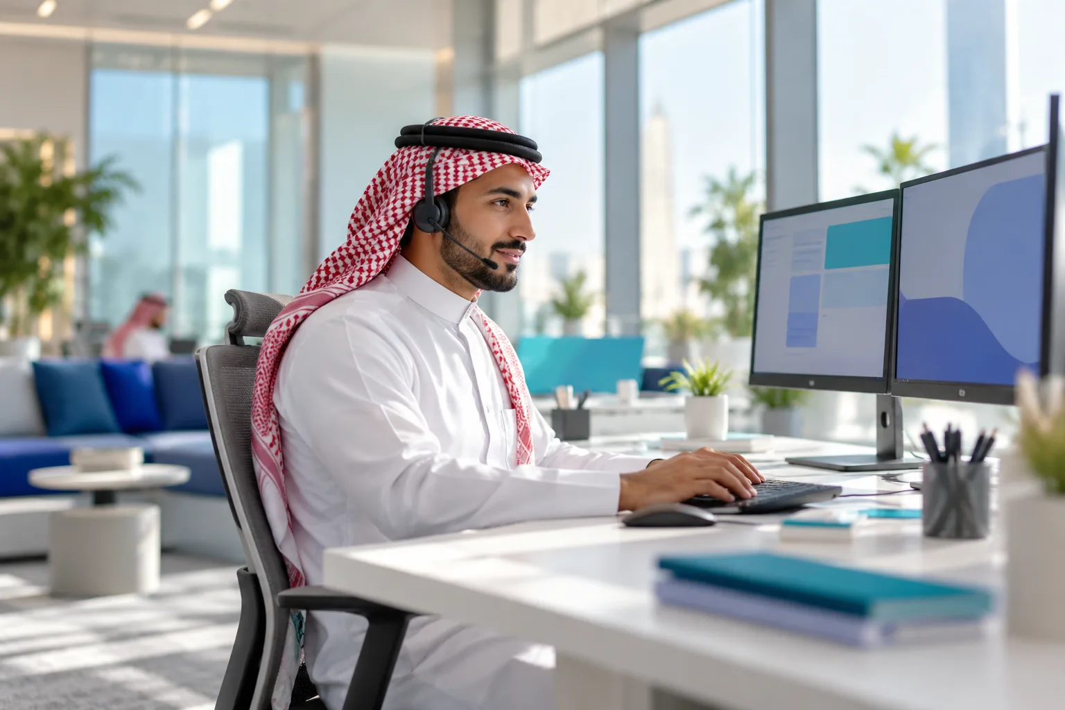 A support agent at a desk in a bright Saudi office handling customer tickets