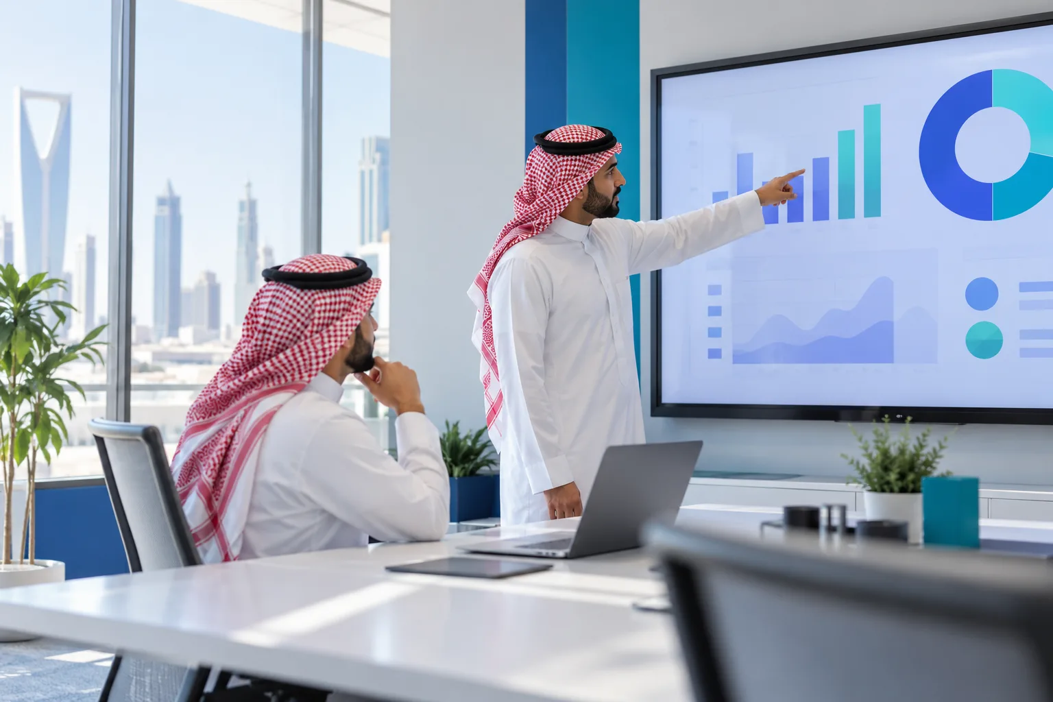 زميلان يراجعان شاشة عرض تحمل رسوماً بيانية مجردة في غرفة اجتماعات